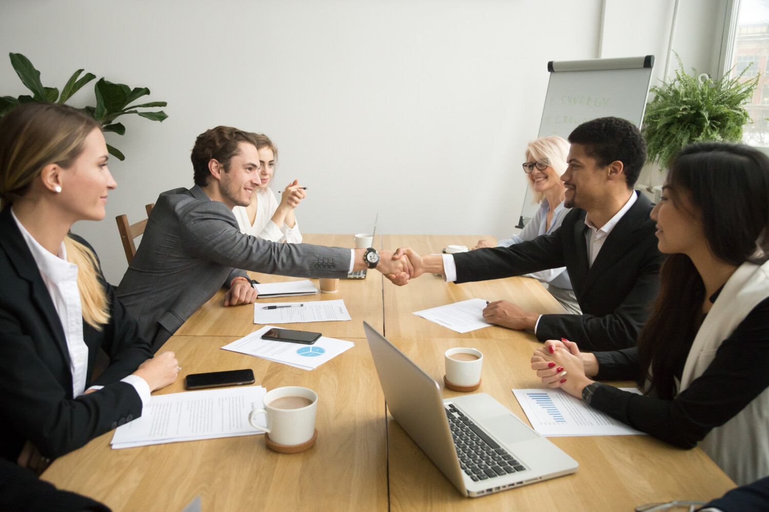 stock-photo-diverse-businessmen-shaking-hands-after-signing-contracts-at-group-multiracial-meeting-african-and-1027563352