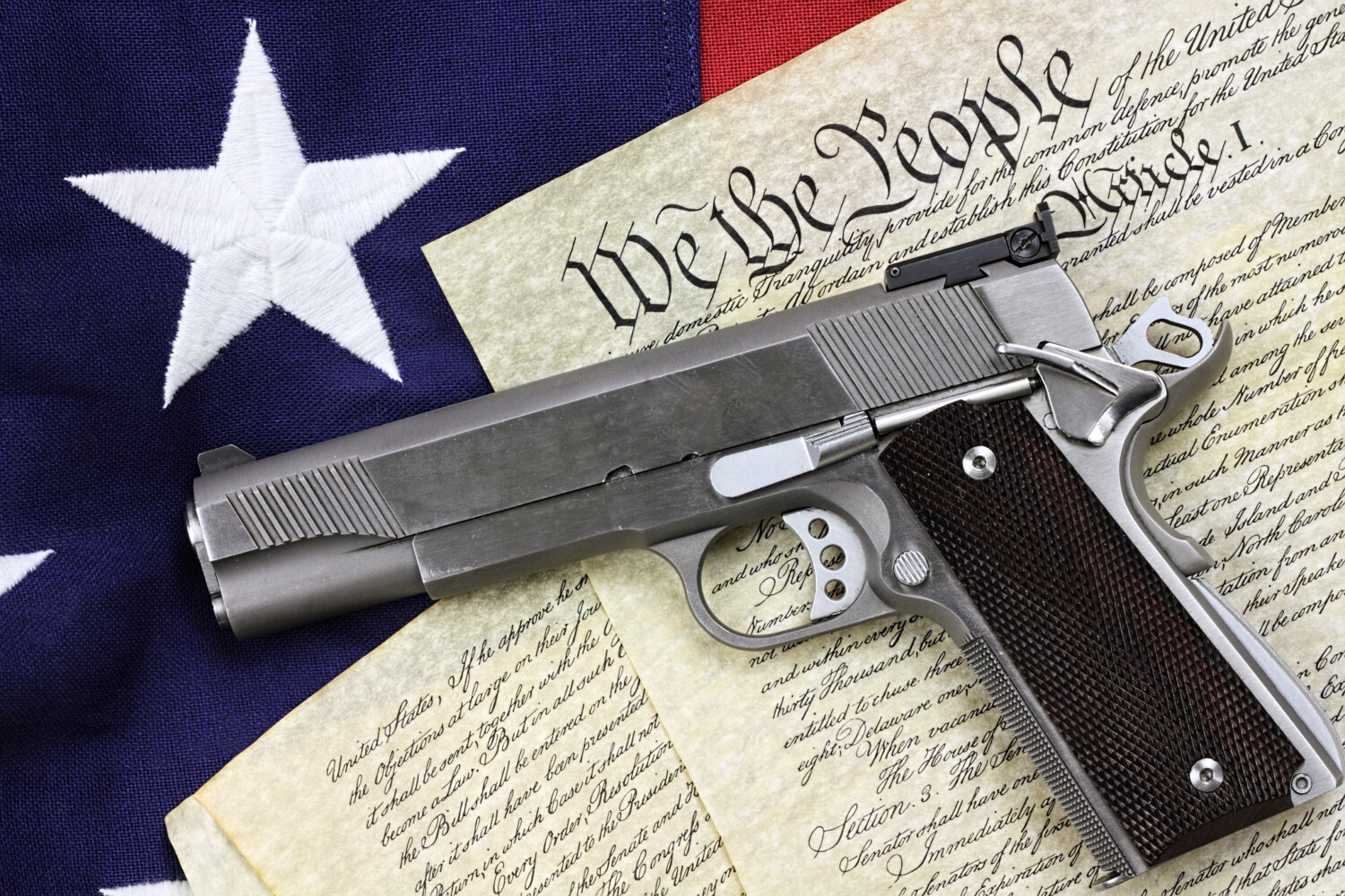 stock-photo-handgun-lying-over-a-copy-of-the-united-states-constitution-and-the-american-flag-129482747